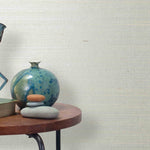End table with a vase, horse sculpture and stones in front of a wall covered in sisal grasscloth in mottled white and cream.