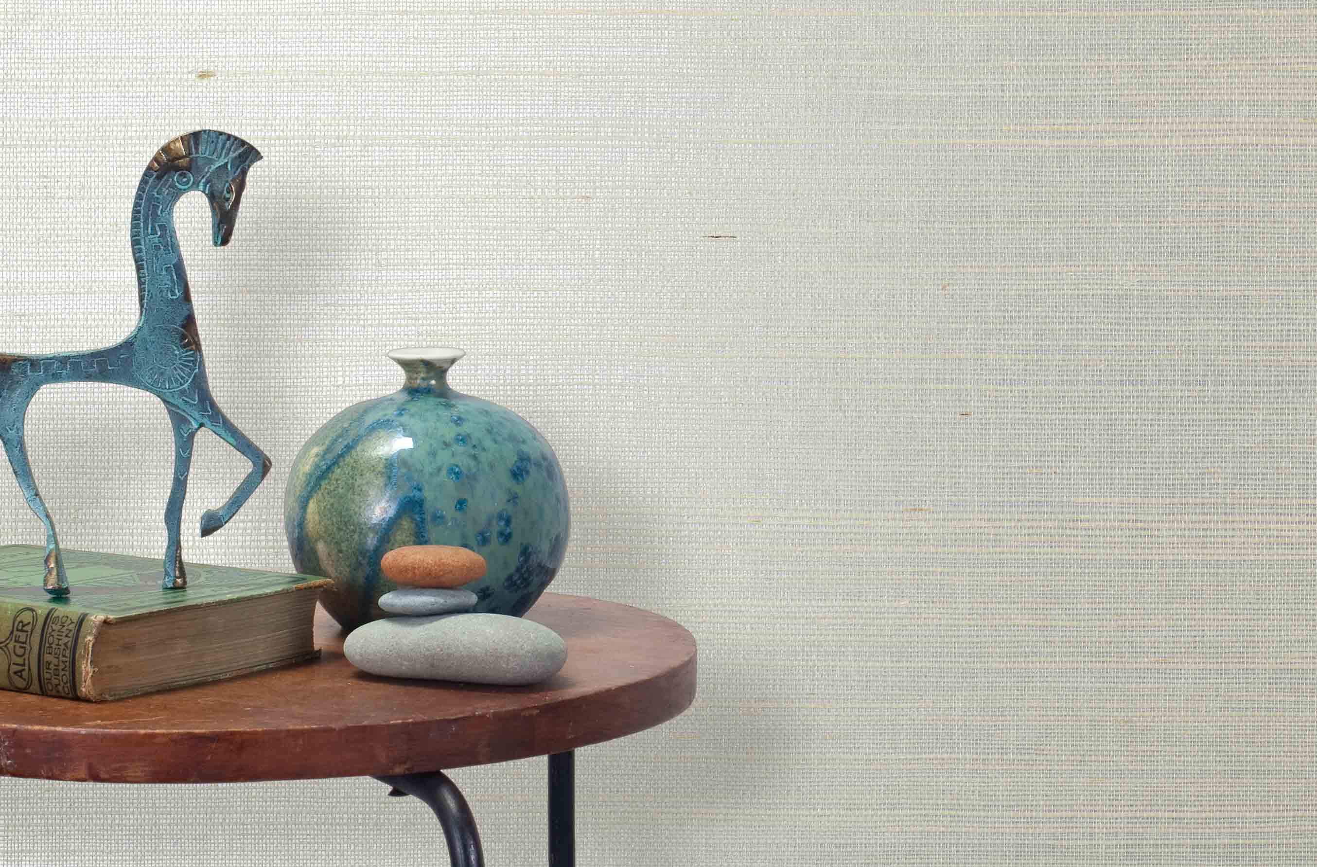 End table with a vase, horse sculpture and stones in front of a wall covered in sisal grasscloth in mottled white and cream.
