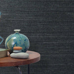 End table with a vase, horse sculpture and stones in front of a wall covered in sisal grasscloth in mottled navy blue.