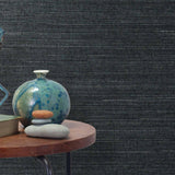 End table with a vase, horse sculpture and stones in front of a wall covered in sisal grasscloth in mottled navy blue.