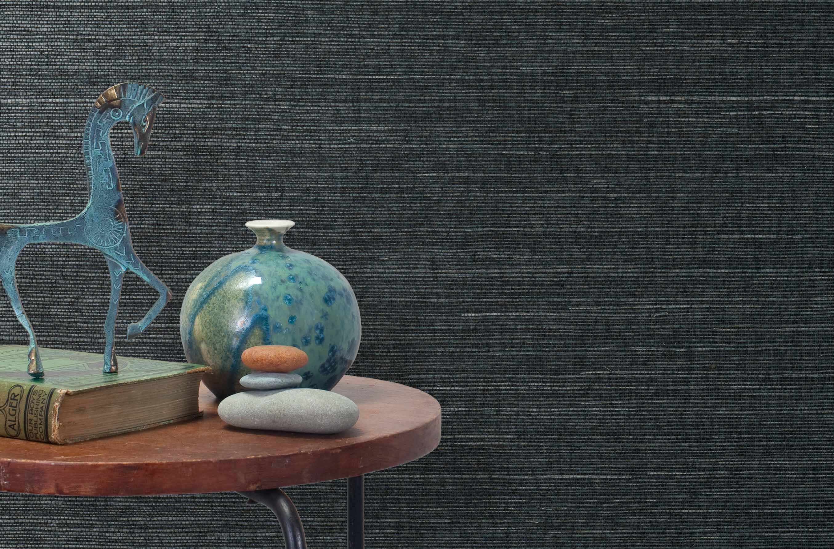 End table with a vase, horse sculpture and stones in front of a wall covered in sisal grasscloth in mottled navy blue.