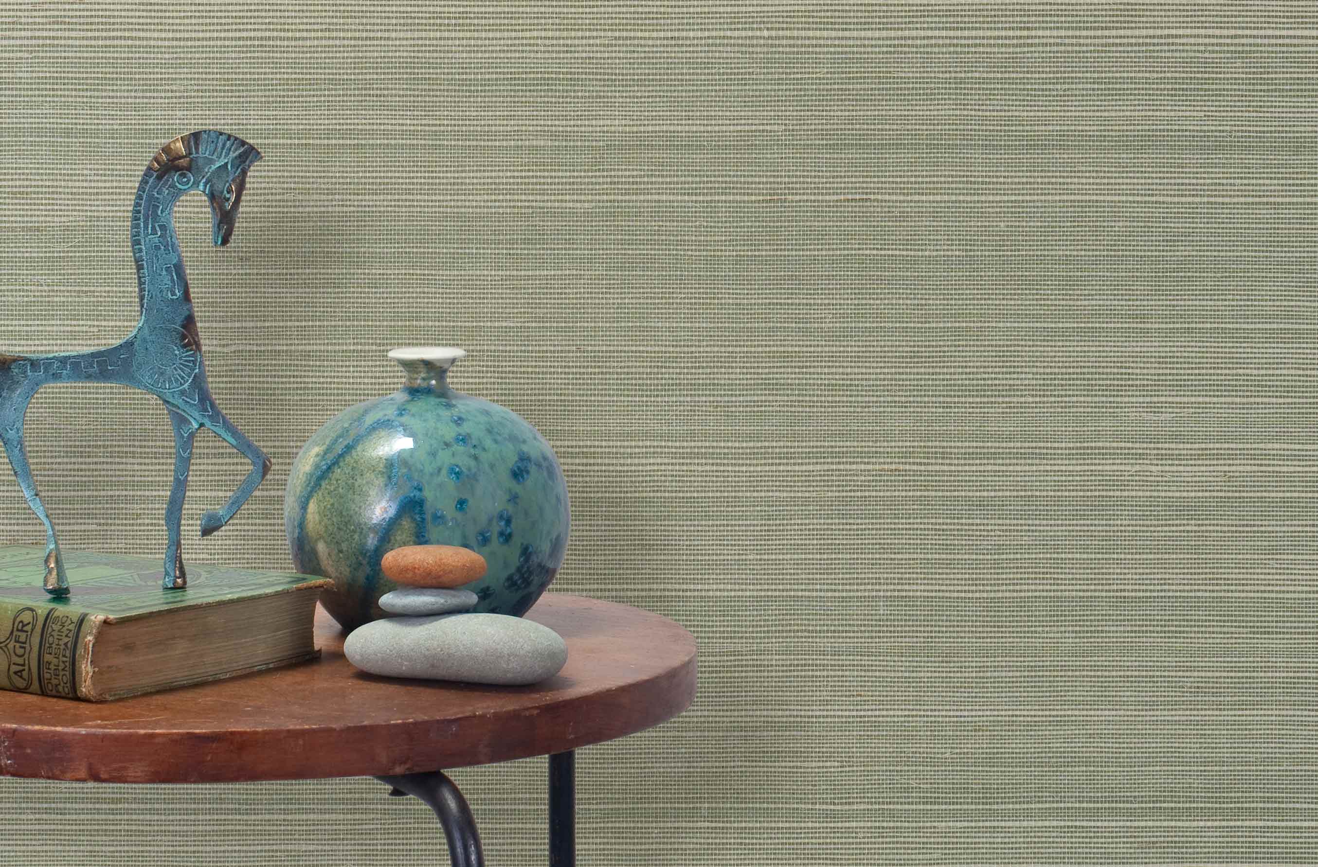 End table with a vase, horse sculpture and stones in front of a wall covered in sisal grasscloth in cream and green.