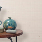 End table with a vase, horse sculpture and stones in front of a wall covered in sisal grasscloth in mottled pink.