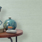 End table with a vase, horse sculpture and stones in front of a wall covered in sisal grasscloth in cream and pastel blue.