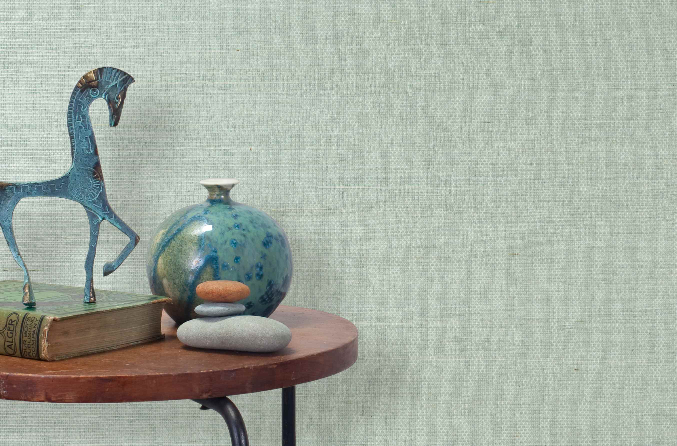 End table with a vase, horse sculpture and stones in front of a wall covered in sisal grasscloth in cream and pastel blue.