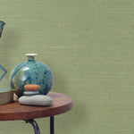 End table with a vase, horse sculpture and stones in front of a wall covered in sisal grasscloth in light green.