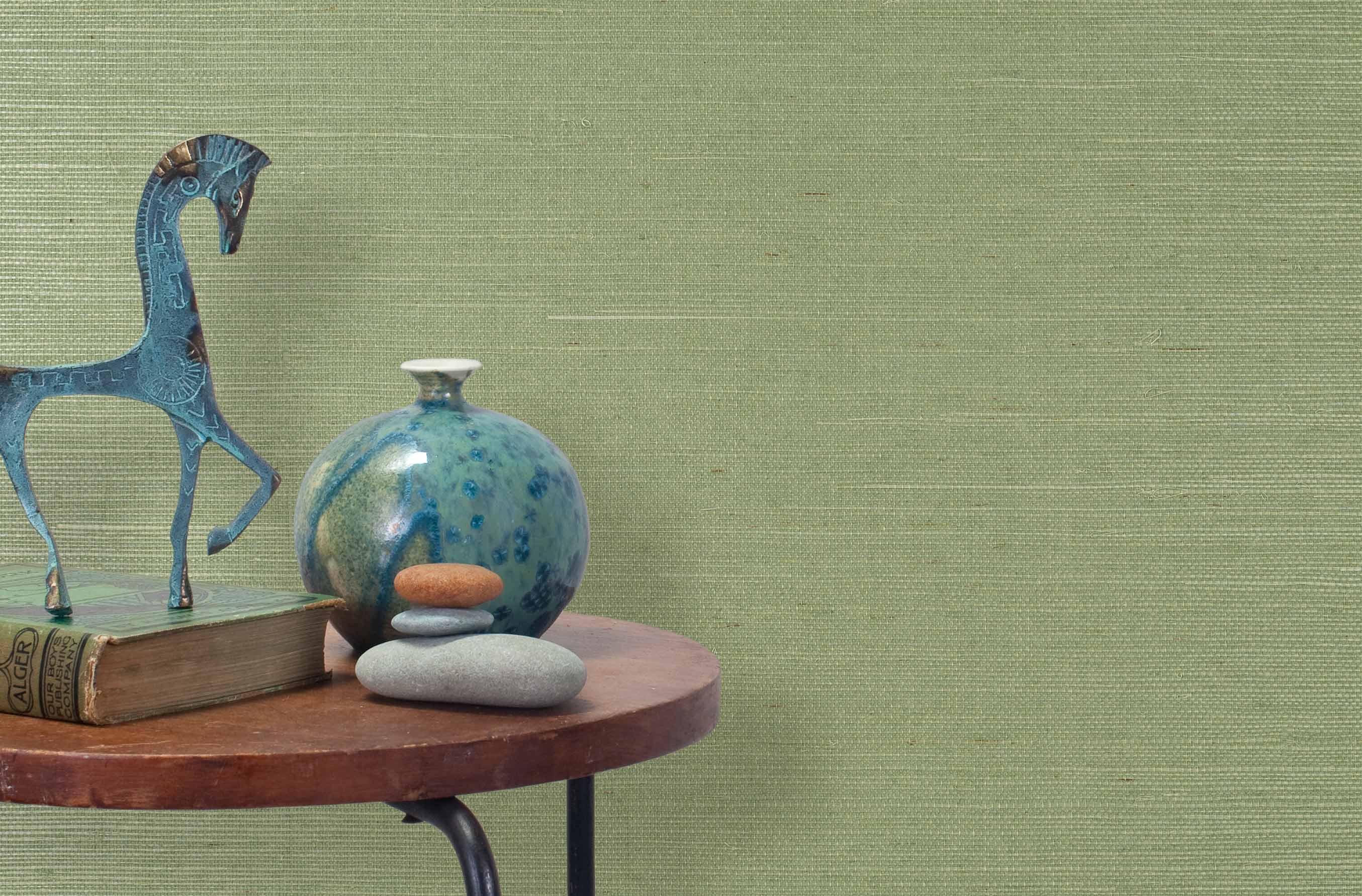 End table with a vase, horse sculpture and stones in front of a wall covered in sisal grasscloth in light green.