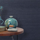 End table with a vase, horse sculpture and stones in front of a wall covered in sisal grasscloth in mottled navy.