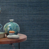 End table with a vase, horse sculpture and stones in front of a wall covered in sisal grasscloth in mottled blue.