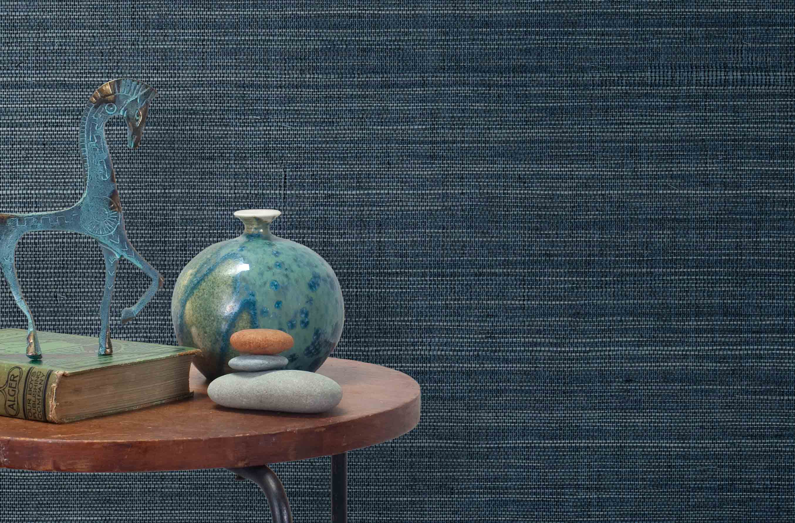 End table with a vase, horse sculpture and stones in front of a wall covered in sisal grasscloth in mottled blue.