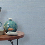End table with a vase, horse sculpture and stones in front of a wall covered in sisal grasscloth in light gray and blue.