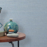 End table with a vase, horse sculpture and stones in front of a wall covered in sisal grasscloth in light gray and blue.