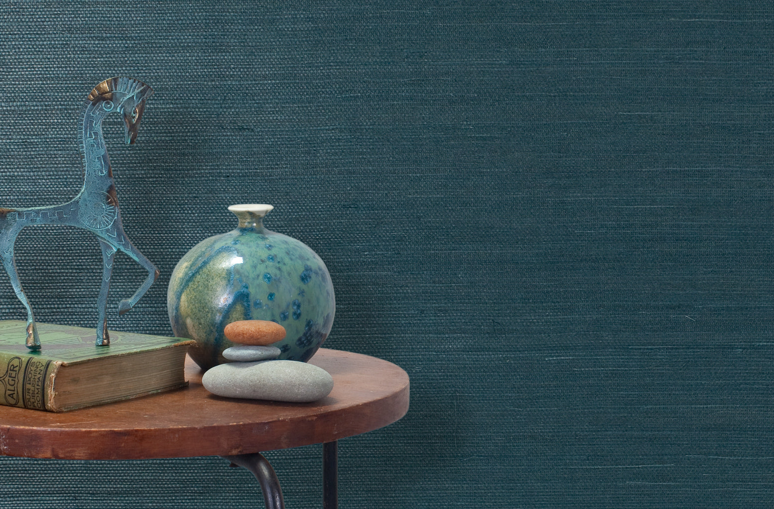 End table with a vase, horse sculpture and stones in front of a wall covered in sisal grasscloth in dark turquoise.