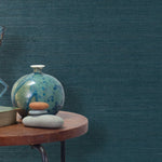 End table with a vase, horse sculpture and stones in front of a wall covered in sisal grasscloth in dark turquoise.