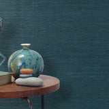 End table with a vase, horse sculpture and stones in front of a wall covered in sisal grasscloth in dark turquoise.