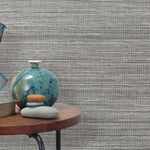 End table with a vase, horse sculpture and stones in front of a wall covered in sisal grasscloth in mottled black and white.