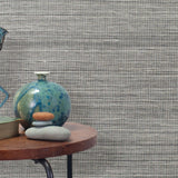 End table with a vase, horse sculpture and stones in front of a wall covered in sisal grasscloth in mottled black and white.