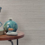 End table with a vase, horse sculpture and stones in front of a wall covered in sisal grasscloth in mottled gray.