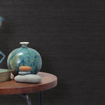 End table with a vase, horse sculpture and stones in front of a wall covered in sisal grasscloth in black.