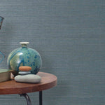 End table with a vase, horse sculpture and stones in front of a wall covered in sisal grasscloth in gray and blue-green.
