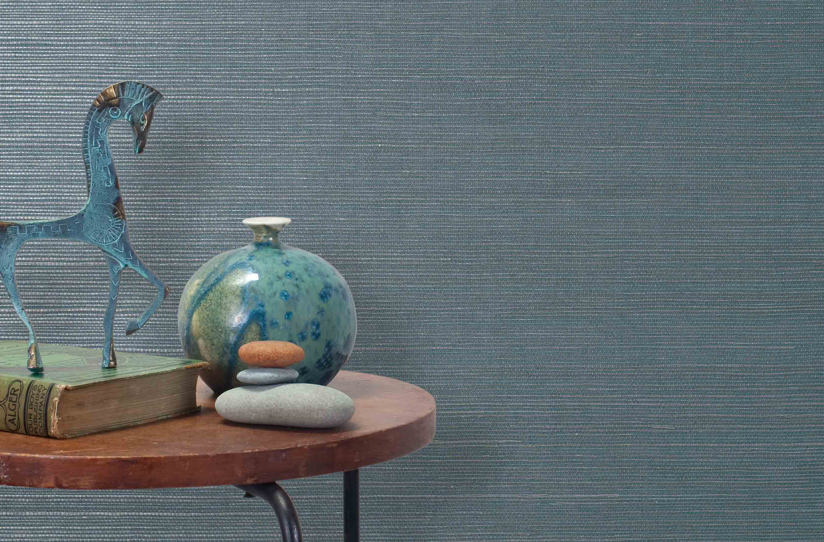 End table with a vase, horse sculpture and stones in front of a wall covered in sisal grasscloth in gray and blue-green.