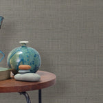 End table with a vase, horse sculpture and stones in front of a wall covered in sisal grasscloth in mottled gray.