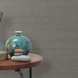 End table with a vase, horse sculpture and stones in front of a wall covered in sisal grasscloth in mottled gray.