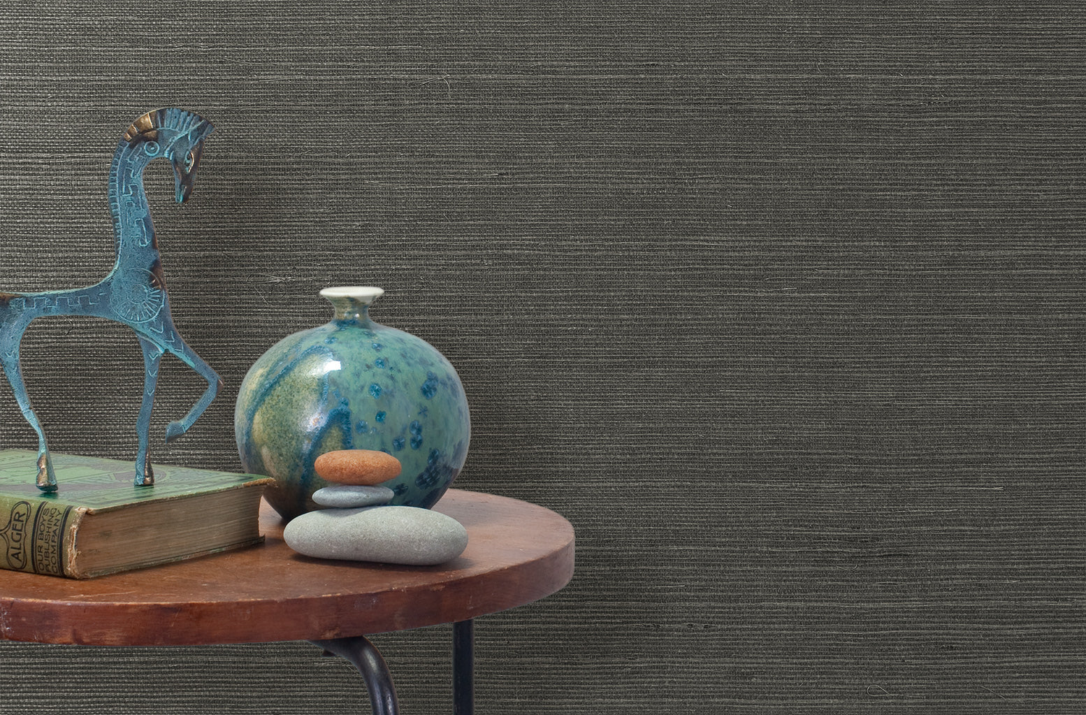 End table with a vase, horse sculpture and stones in front of a wall covered in sisal grasscloth in mottled gray.