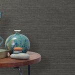 End table with a vase, horse sculpture and stones in front of a wall covered in sisal grasscloth in mottled gray.