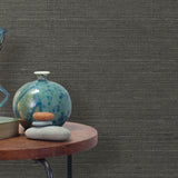 End table with a vase, horse sculpture and stones in front of a wall covered in sisal grasscloth in mottled gray.