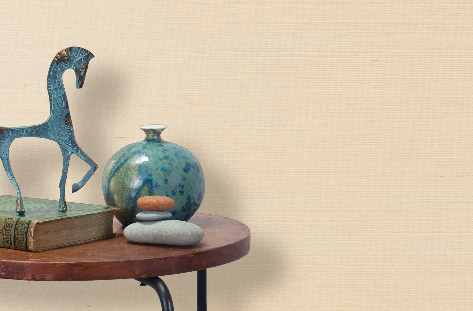 End table with a vase, horse sculpture and stones in front of a wall covered in sisal grasscloth in cream.