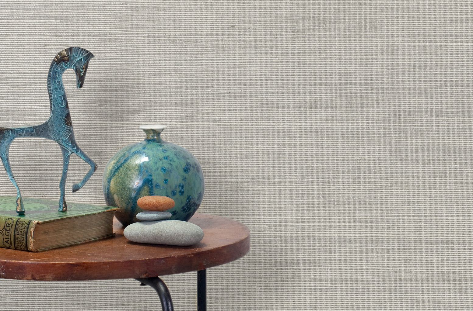 End table with a vase, horse sculpture and stones in front of a wall covered in sisal grasscloth in white and gray.