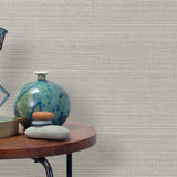 End table with a vase, horse sculpture and stones in front of a wall covered in sisal grasscloth in white and gray.