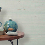 End table with a vase, horse sculpture and stones in front of a wall covered in sisal grasscloth in mottled pale blue.