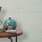 End table with a vase, horse sculpture and stones in front of a wall covered in sisal grasscloth in mottled pale blue.