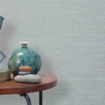 End table with a vase, horse sculpture and stones in front of a wall covered in sisal grasscloth in mottled blue-gray.
