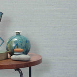 End table with a vase, horse sculpture and stones in front of a wall covered in sisal grasscloth in mottled blue-gray.