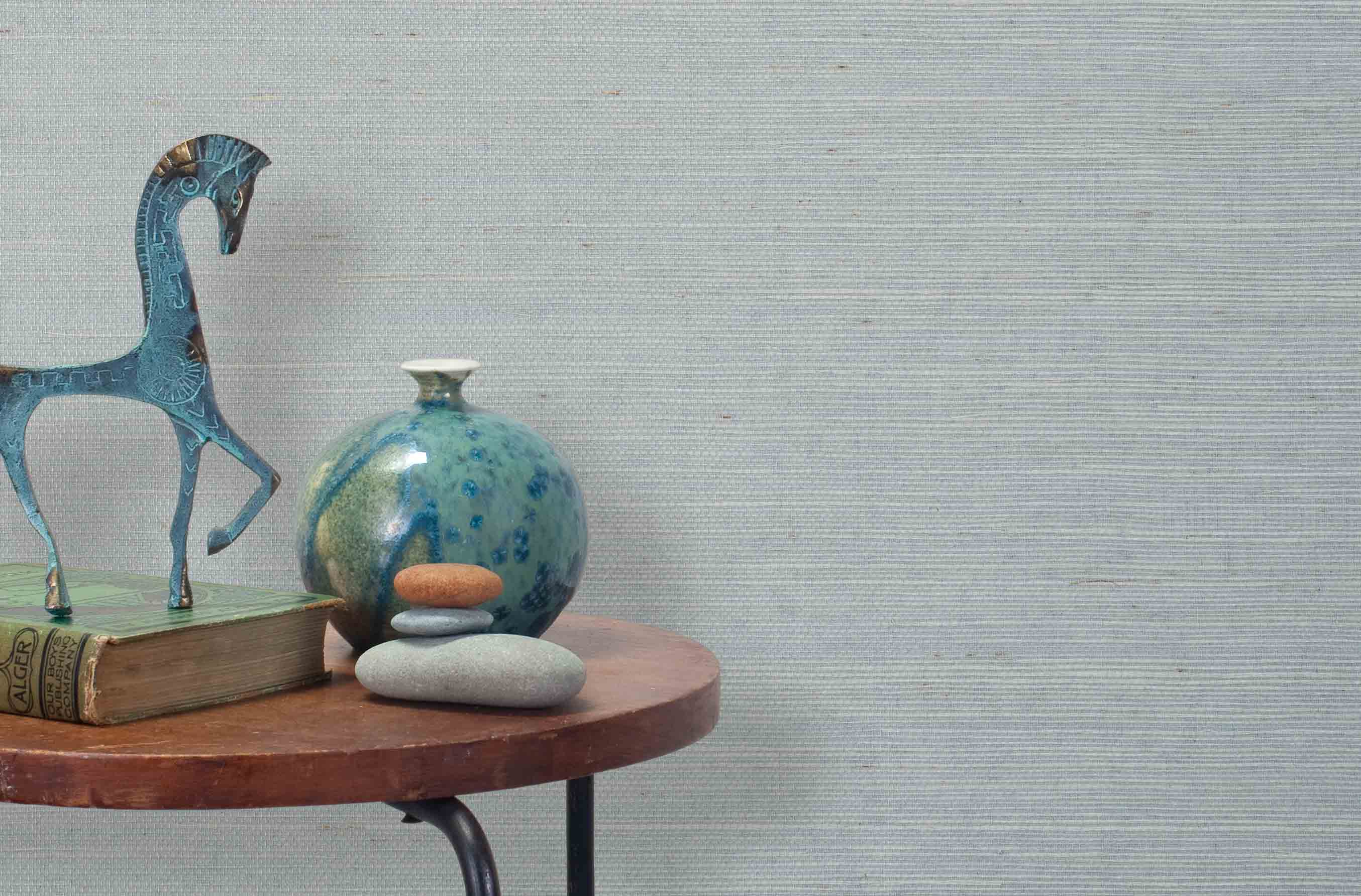End table with a vase, horse sculpture and stones in front of a wall covered in sisal grasscloth in mottled blue-gray.