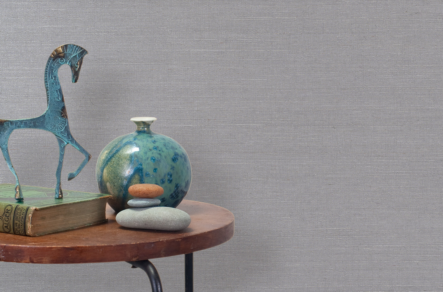 End table with a vase, horse sculpture and stones in front of a wall covered in sisal grasscloth in metallic gray.