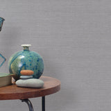 End table with a vase, horse sculpture and stones in front of a wall covered in sisal grasscloth in metallic gray.