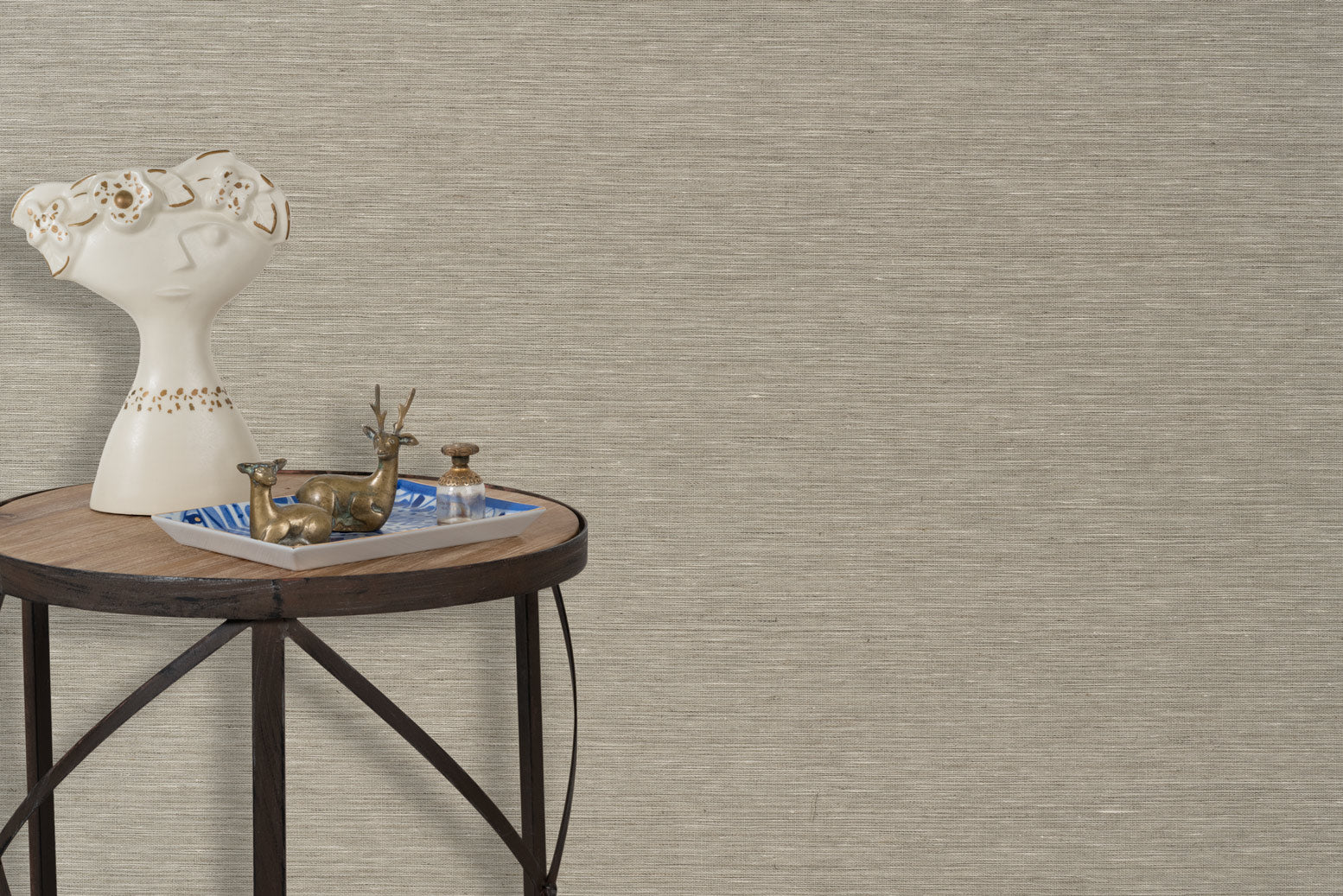 End table with a tray and some sculptures in front of a wall papered in textured grasscloth in a neutral shade.