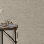 End table with a tray and some sculptures in front of a wall papered in textured grasscloth in a neutral shade.