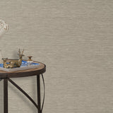 End table with a tray and some sculptures in front of a wall papered in textured grasscloth in a neutral shade.