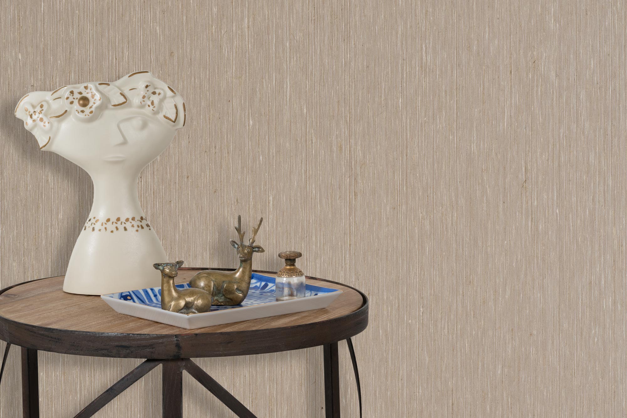 End table with a tray and some sculptures in front of a wall papered in textured grasscloth in brown.