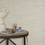 End table with a tray and some sculptures in front of a wall papered in textured grasscloth in cream. 