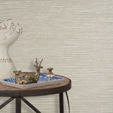 End table with a tray and some sculptures in front of a wall papered in textured grasscloth in cream. 