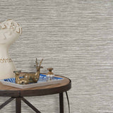 End table with a tray and some sculptures in front of a wall papered in textured grasscloth in black and white.