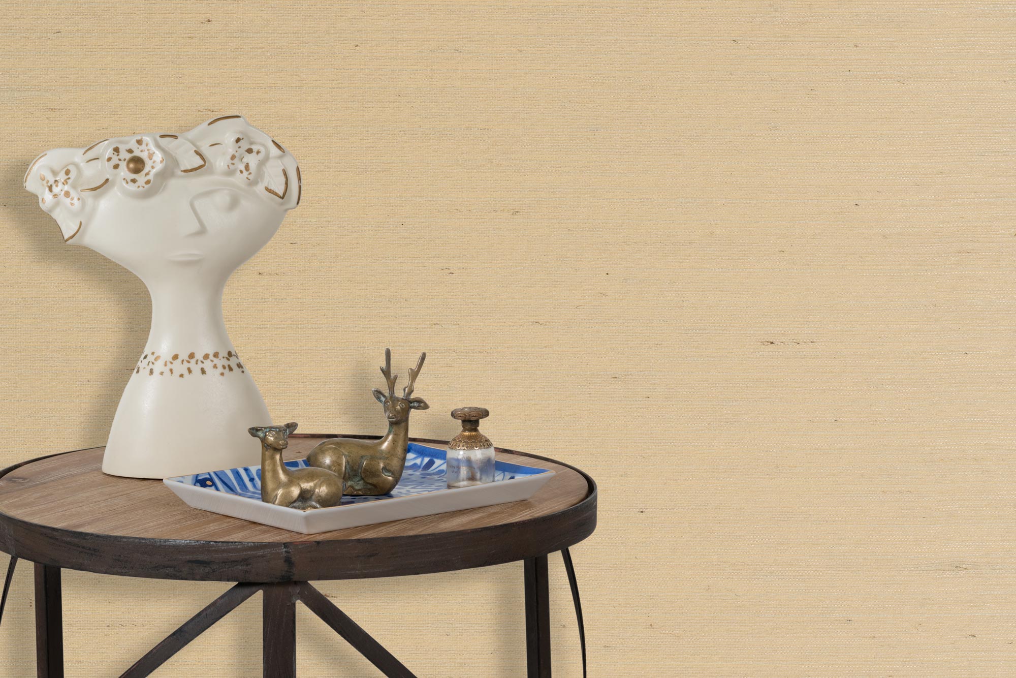 End table with a tray and some sculptures in front of a wall papered in textured grasscloth in cream. 