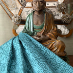 Sculpture of Buddha against antique mirror with draped blue greek key fabric.