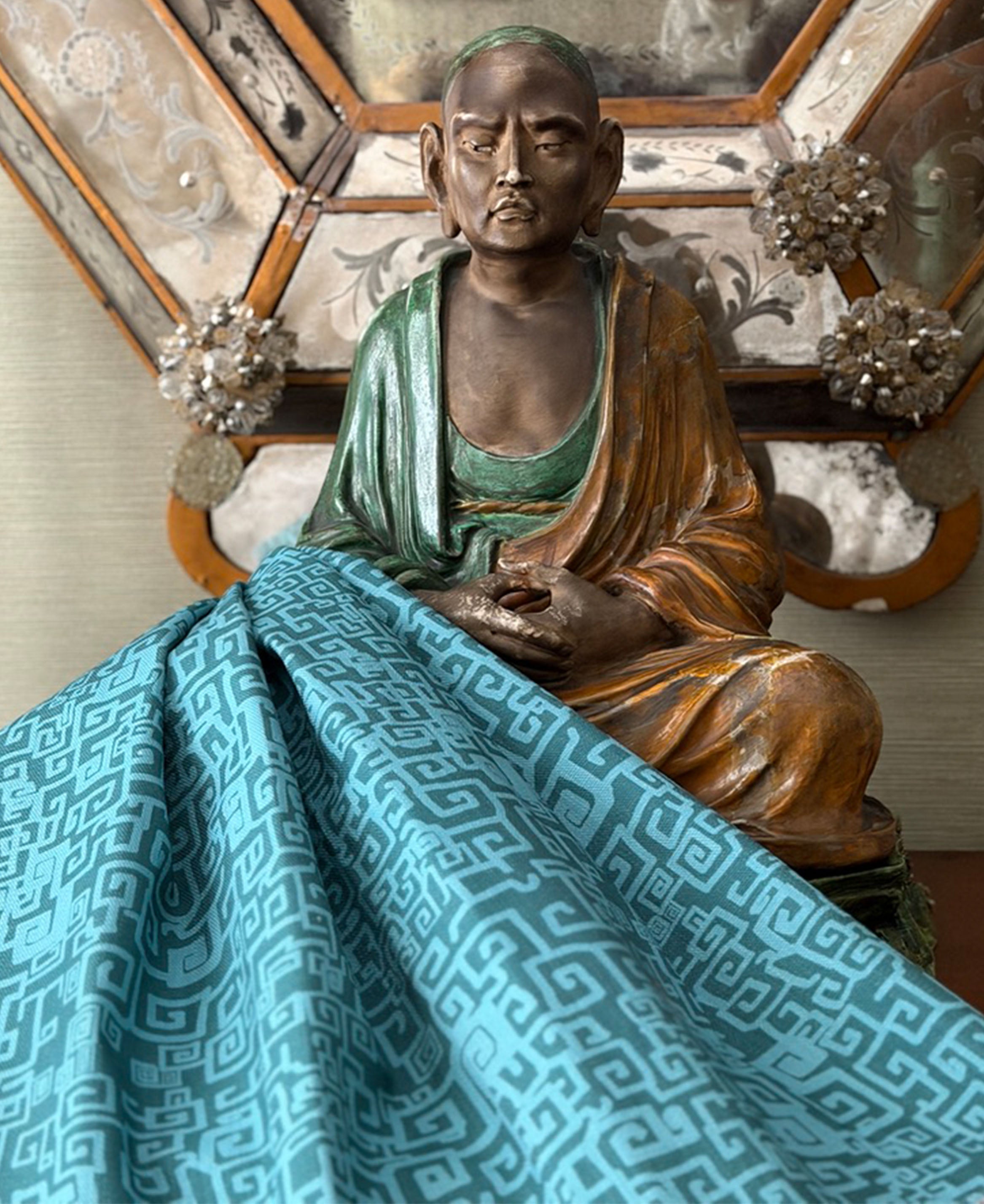Sculpture of Buddha against antique mirror with draped blue greek key fabric.